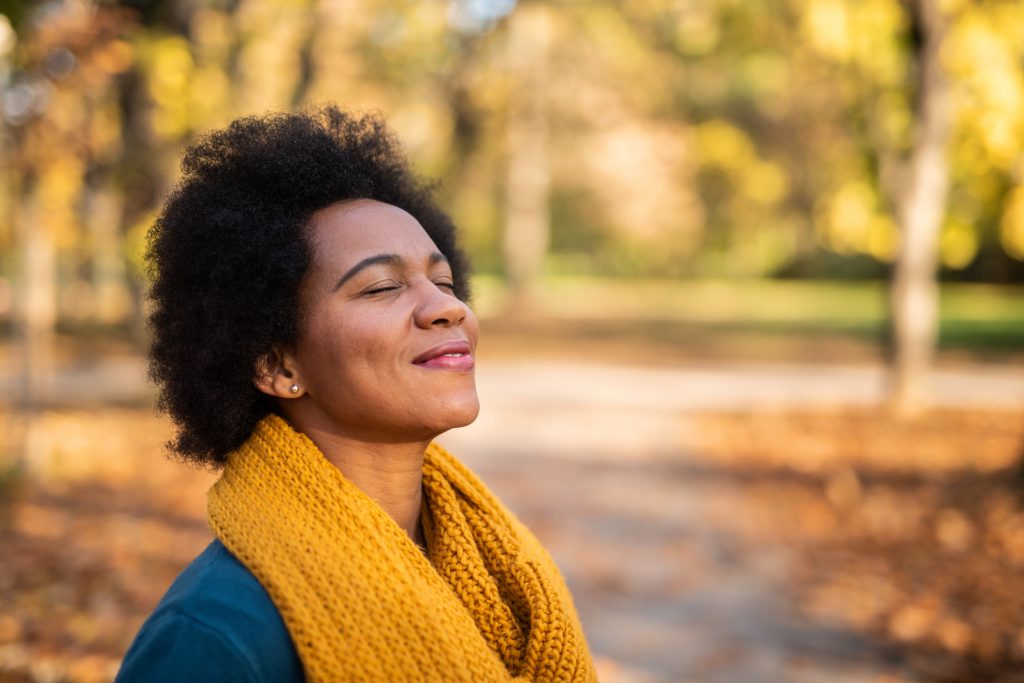 Young woman smiling with gratitude in a park surrounded by vibrant fall foliage, symbolizing thankfulness and personal growth