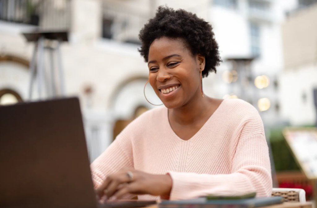 Smiling woman working on laptop outside, exploring franchise opportunities with SYNERGY HomeCare